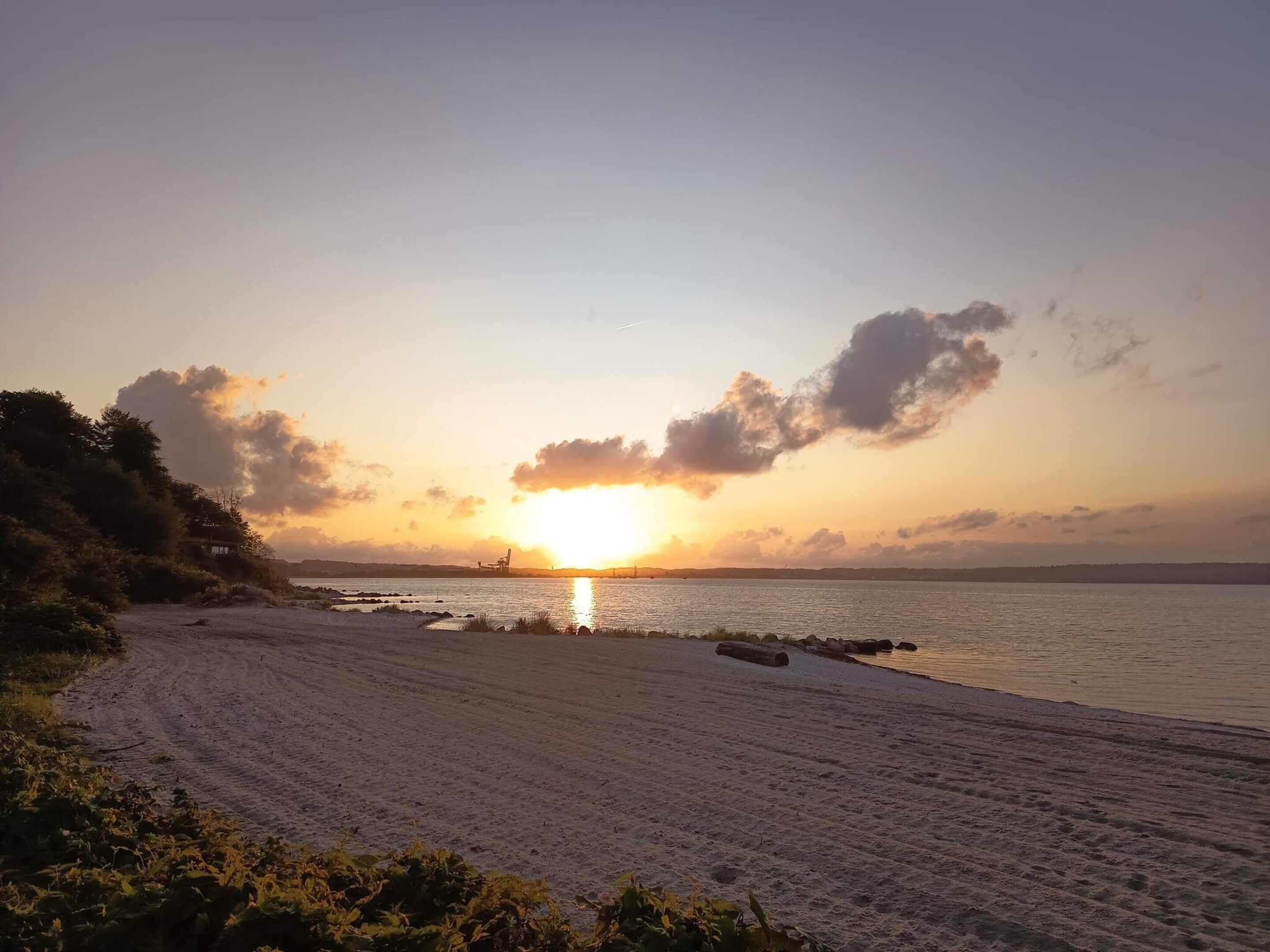 A beach with a sunset, clear sky, and calm water.