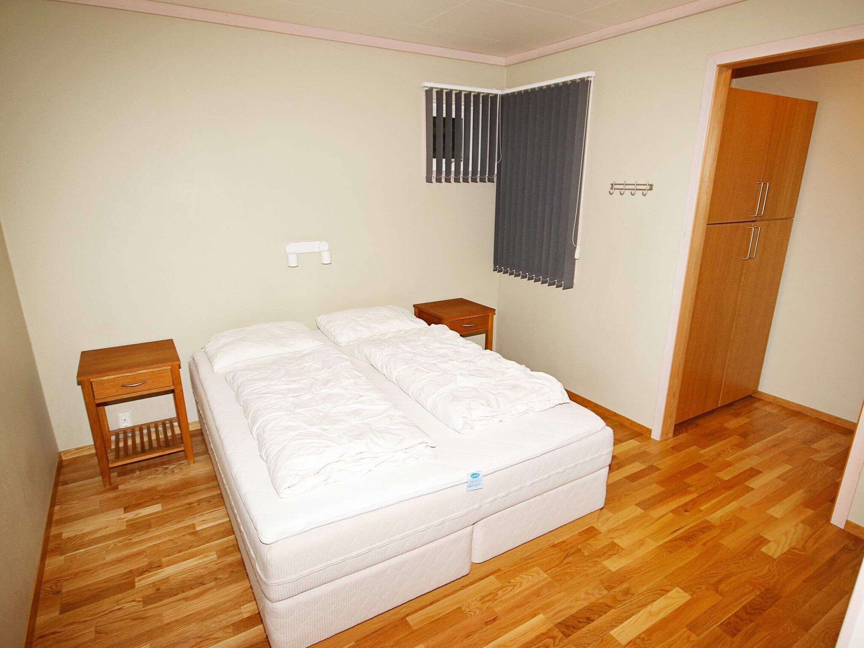 Une chambre à coucher avec un lit double, une table de chevet en bois, une petite table de chevet et une armoire.