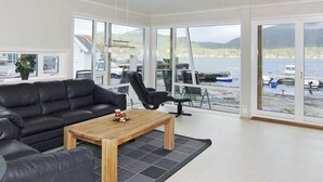 A modern living room with a black leather sofa, a wooden coffee table, and a black office chair. Large windows offer a view of boats and a body of water. - 5 Star Holiday Home in Jelsa (Suldal)