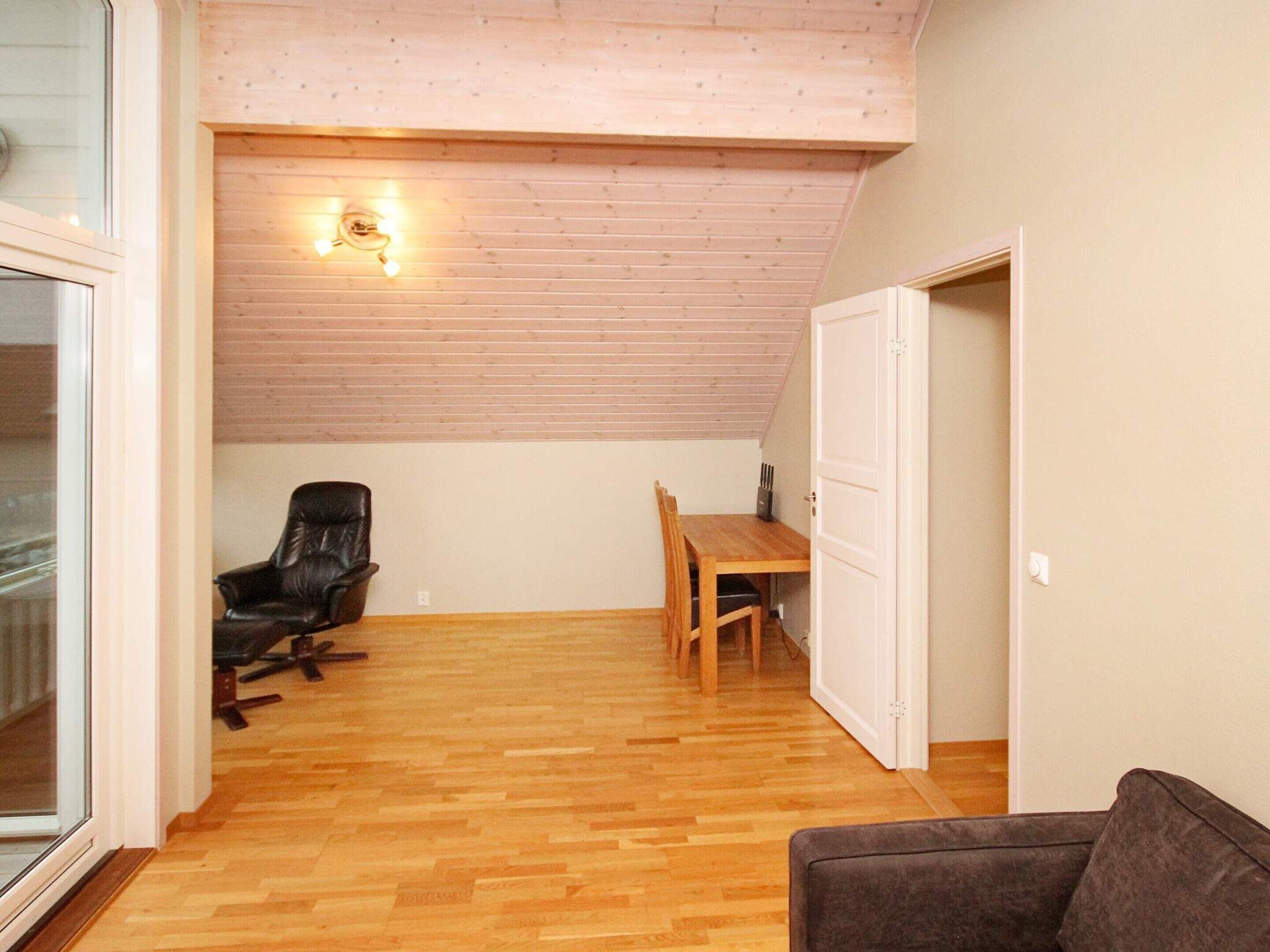 A room with a wooden floor, a black leather chair, a wooden dining table, and a white door.