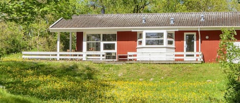 A red building with a white porch, surrounded by a grassy field with yellow flowers.