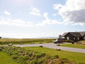 A coastal property with a gravel driveway leading to a black building, a car parked in front, and a bench by the path.