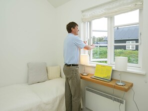 A person standing by a window, a bed, and a desk with a laptop and a lamp. - 5 Star Holiday Home in Nysted (Nysted)