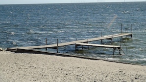 En sandstrand med en träbrygga som sträcker sig ut i vattnet.