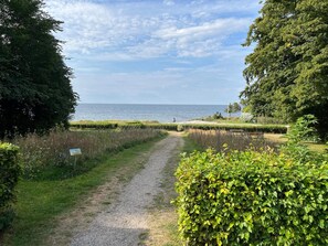 A gravel path leading to a beach with a clear view of the sea and a person cycling in the distance. - 5 Star Holiday Home in Nysted (Nysted)