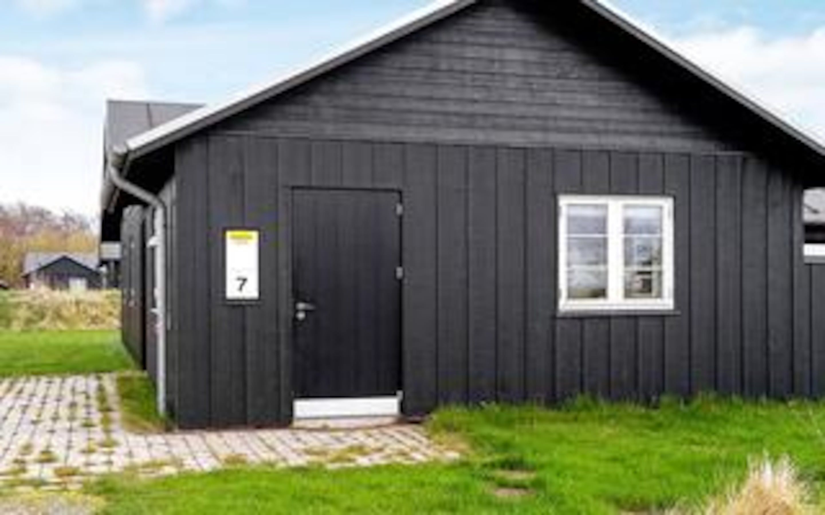 En sort bygning med en dør markeret '7', et vindue og en belagt indgang.