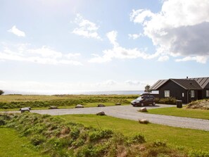 A coastal property with a gravel driveway leading to a black building, a car parked in front, and a bench in the foreground. - 5 Star Holiday Home in Nysted (Nysted)