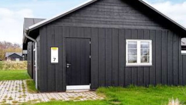 A black building with a door marked '7', a window, and a paved entrance. - 5 Star Holiday Home in Nysted (Nysted)