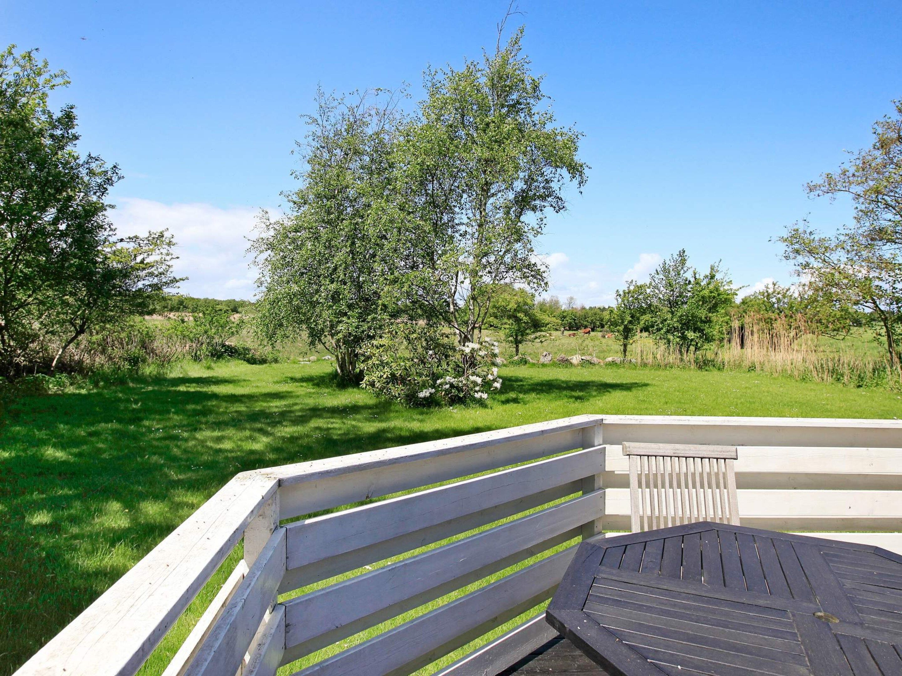 A wooden bench with a slatted design, positioned in a grassy outdoor area with trees and a clear sky.