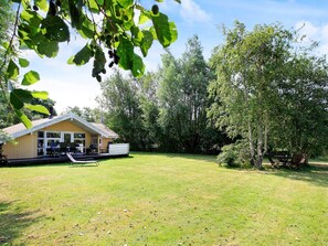 A wooden cabin with a patio, surrounded by a grassy yard and trees. - 6 Person Holiday Home in Humble (Sydlangeland)