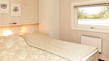 A room with a bed, a window, a wall-mounted shelf with pictures, and a white wardrobe.