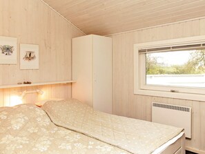 A room with a bed, a window, a wall-mounted shelf with pictures, and a white wardrobe.