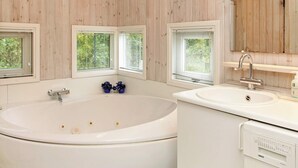 Ein Badezimmer mit einer großen Badewanne, einem Waschbecken und drei Fenstern mit Jalousien.
