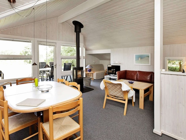 A cozy room with a round table, chairs, a sofa, a TV, and a wood-burning stove.