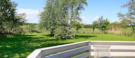A wooden deck with a bench and a table, surrounded by greenery and trees.