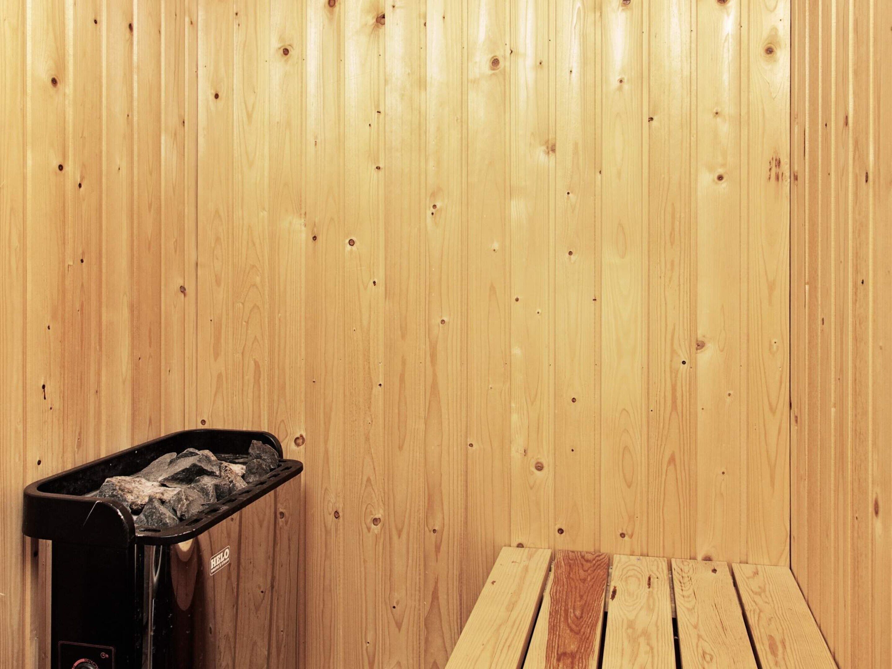 A sauna room with a wooden wall, a bench, and a heater.