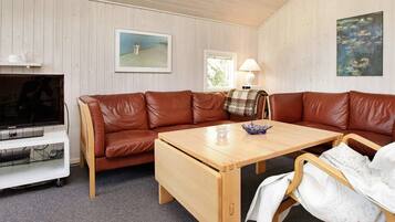 A cozy living room with a brown leather sofa, a wooden coffee table, a television, and a lamp.