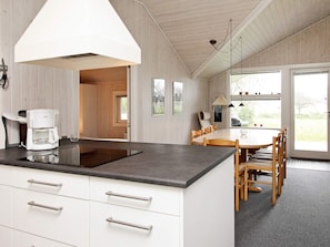 Een moderne keuken met een ingebouwde kookplaat, witte kasten en een eethoek met een houten tafel en stoelen.