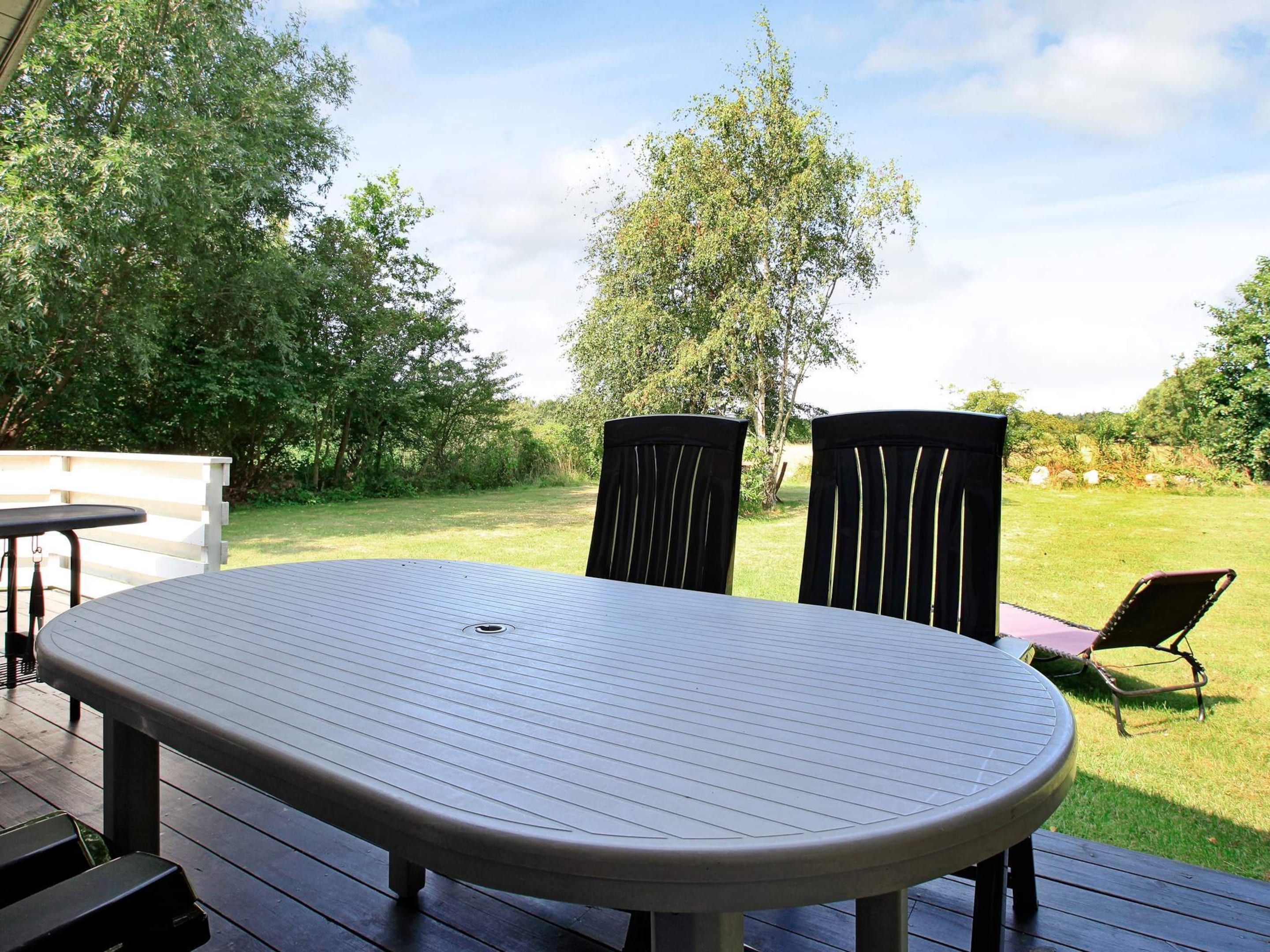 Eine Terrasse im Freien mit einem runden Tisch und zwei Stühlen, umgeben von einer Rasenfläche und Bäumen.