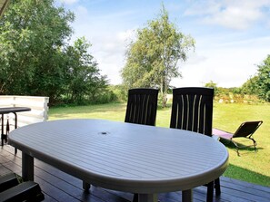 Een terras buiten met een ronde tafel en twee stoelen, omgeven door een gazon en bomen.