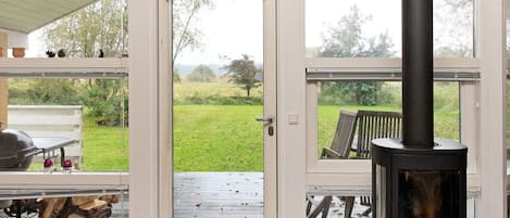 A room with a wood-burning stove, a door leading to an outdoor area with a bench, and a basket of firewood.