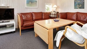 Un salon chaleureux avec un canapé en cuir marron, une table basse en bois, un téléviseur et une lampe.