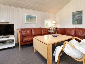 Un salon chaleureux avec un canapé en cuir marron, une table basse en bois, un téléviseur et une lampe.