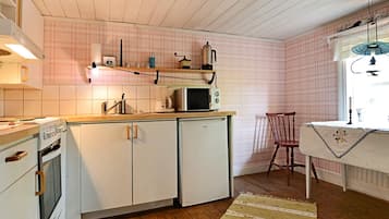Cocina funcional con alacenas blancas, microondas y estufa. Suelo de madera y una silla cerca de una ventana.