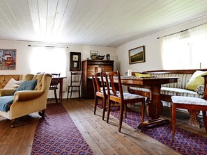 A cozy living room with a wooden floor, a patterned rug, a sofa, a dining table with chairs, and a piano. - 5 Person Holiday Home in Jonkoping (Jonkoping)
