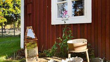 A rustic outdoor setting with a red wooden wall, a window with a flower, a metal lantern, and a wooden trough.