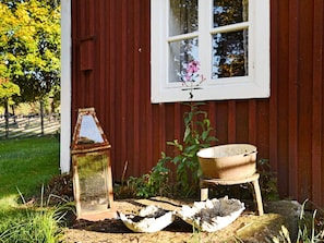 A rustic outdoor setting with a red wooden wall, a window with a flower, a metal lantern, and a wooden trough. - 5 Person Holiday Home in Jonkoping (Jonkoping)