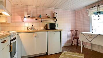 Una cocina compacta con armarios blancos, microondas, estufa y piso de madera.