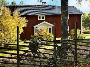 A red barn with a white door and windows, surrounded by a wooden fence and trees. - 5 Person Holiday Home in Jonkoping (Jonkoping)
