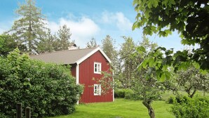 A red barn with a sloped roof, surrounded by lush green grass and trees. - 5 Person Holiday Home in Jonkoping (Jonkoping)