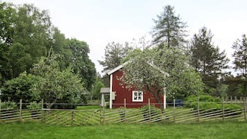 A red barn with a white door and window, surrounded by a wooden fence and lush green trees.