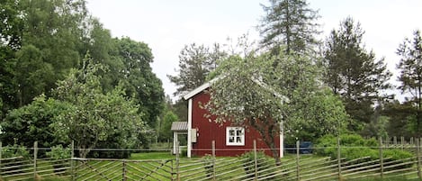 A red barn with a white door and window, surrounded by a wooden fence and lush green trees.