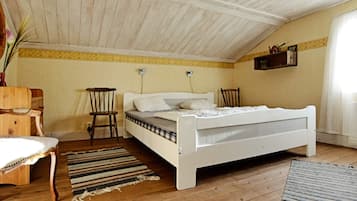 A bedroom with a sloped ceiling, a bed, a chair, a small table, and a wall-mounted shelf.