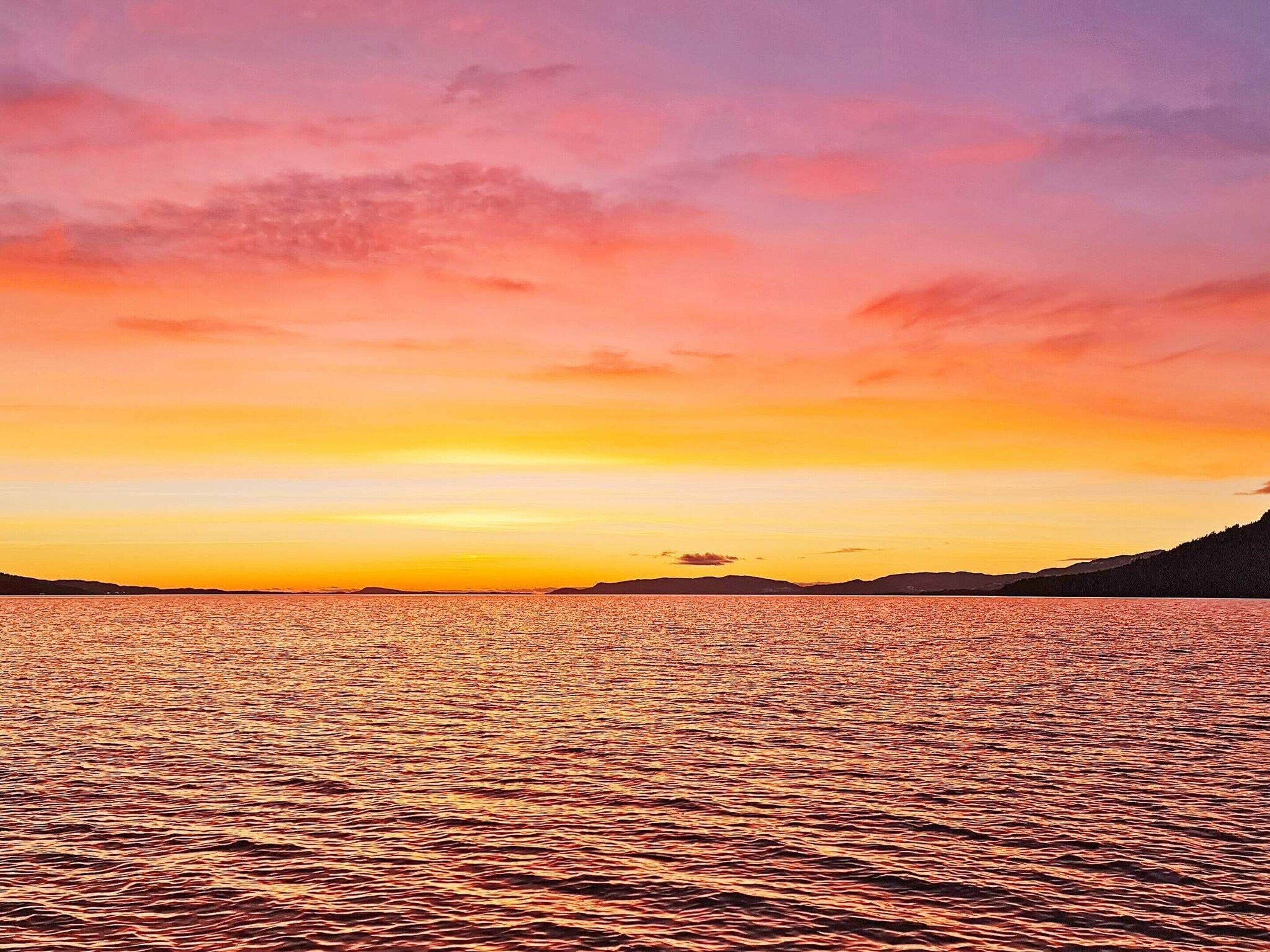 A sunset over a calm sea with distant land silhouettes.