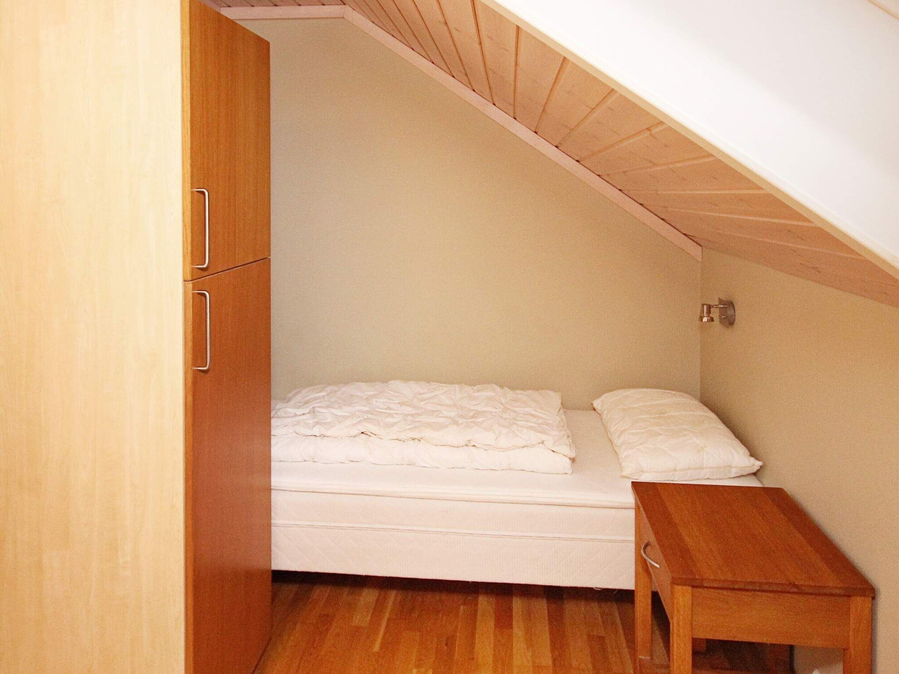 A small, single-bed room with a wooden wardrobe and a small bedside table.