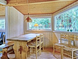 Interior de madera con una mesa, sillas, una lámpara colgante y una ventana que da a vistas de árboles.