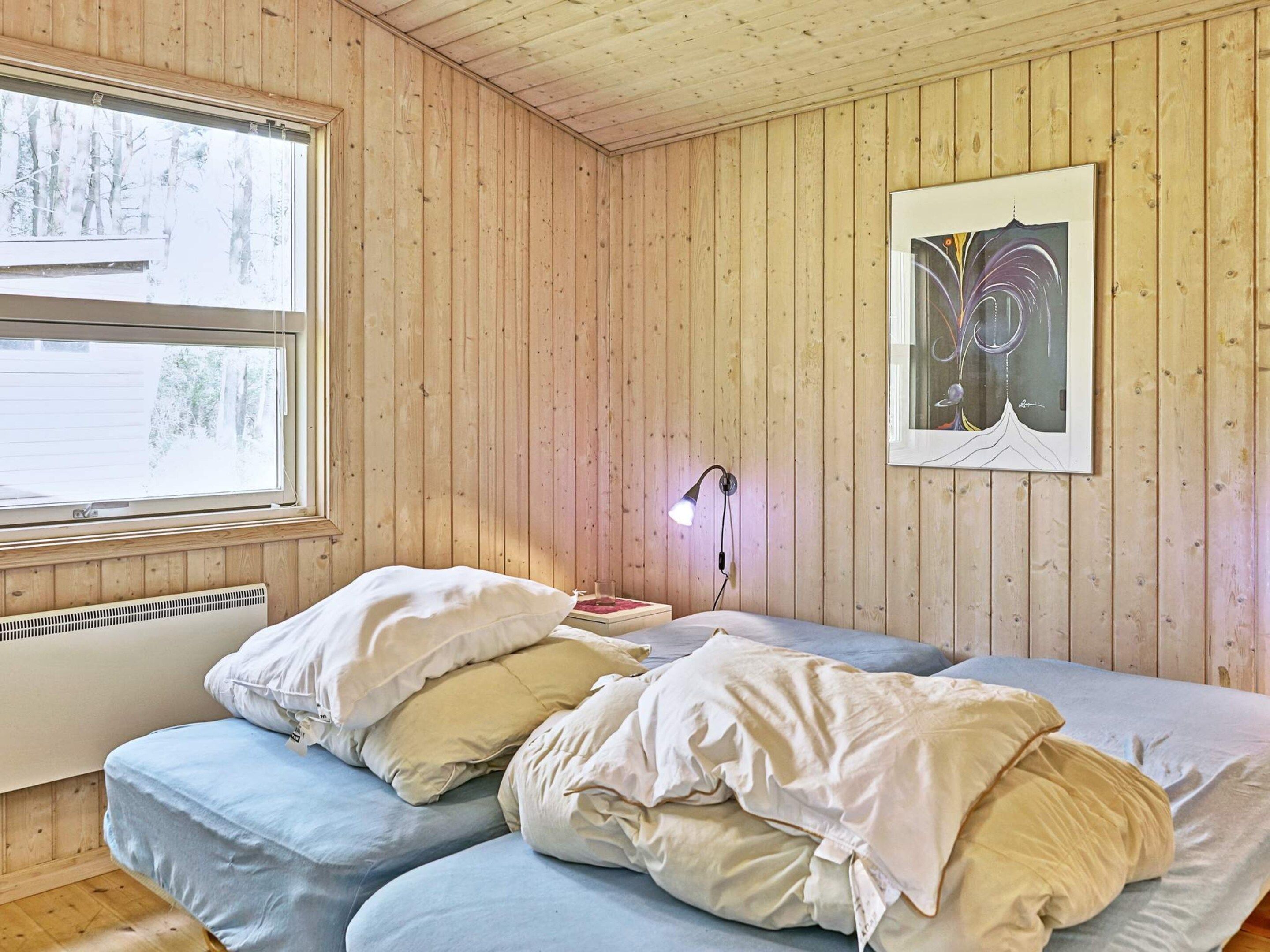 Une pièce aux murs en bois, un lit avec une literie blanche et bleue, un tableau encadré au mur et une fenêtre donnant sur des arbres.