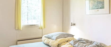 A bedroom with two beds, a window with curtains, a door, and a framed picture on the wall.
