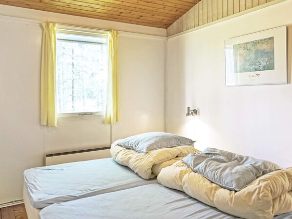 Un dormitori amb dos llits, una finestra amb cortines, una porta i un quadre al mur.