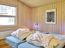 Una habitación con paredes de madera, una cama con almohadas, una mesita de noche, una lámpara y un cuadro en la pared.