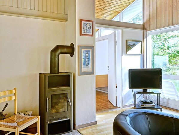 Una sala de estar acogedora con una estufa de leña, un sillón cómodo, un televisor y cuadros en la pared.