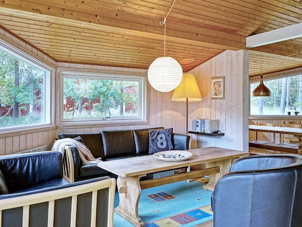 Un acogedor interior de cabaña con techo de madera, un ventanal grande, una mesa de comedor y un sofá.