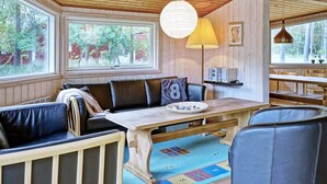 A cozy cabin interior with a wooden ceiling, a large window, a dining table, and a sofa. - Cozy Holiday Home in Aakirkeby Bornholm near Sea (Akirkeby)