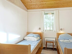 A room with two wooden beds, a window with white curtains, a small wooden stool, and a radiator. - Cozy Holiday Home in Aakirkeby Bornholm near Sea (Akirkeby)