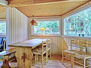 A wooden interior with a table and chairs, a hanging lamp, and large windows with a view of greenery. - Cozy Holiday Home in Aakirkeby Bornholm near Sea (Akirkeby)