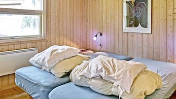Una habitación con paredes de madera, una cama con almohadas, una mesita de noche, una lámpara y un cuadro en la pared.